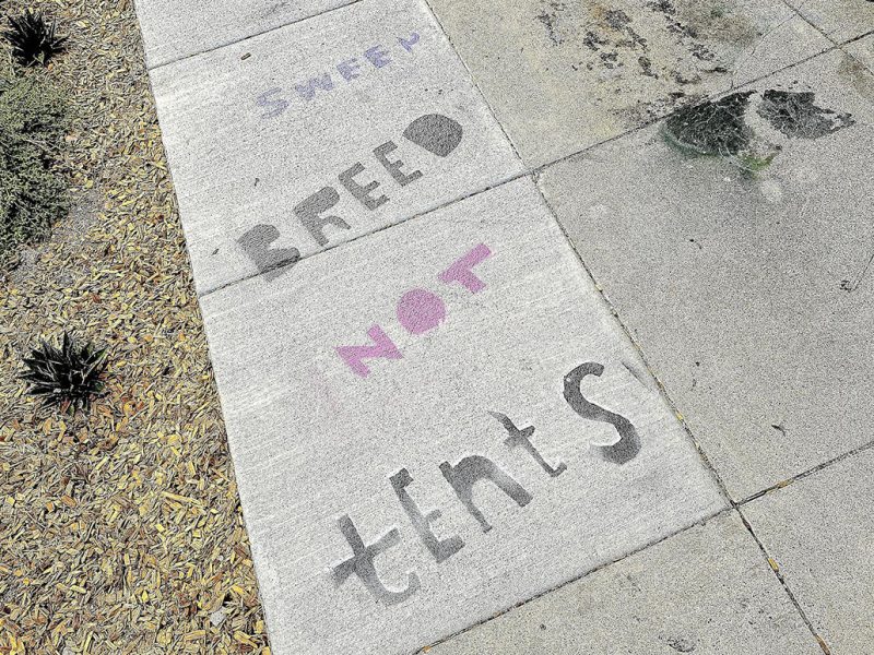 Stenciling on the sidewalk that says sweep Breed not tents.