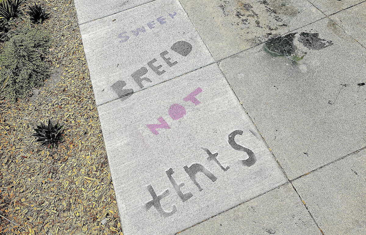 Stenciling on the sidewalk that says sweep Breed not tents.