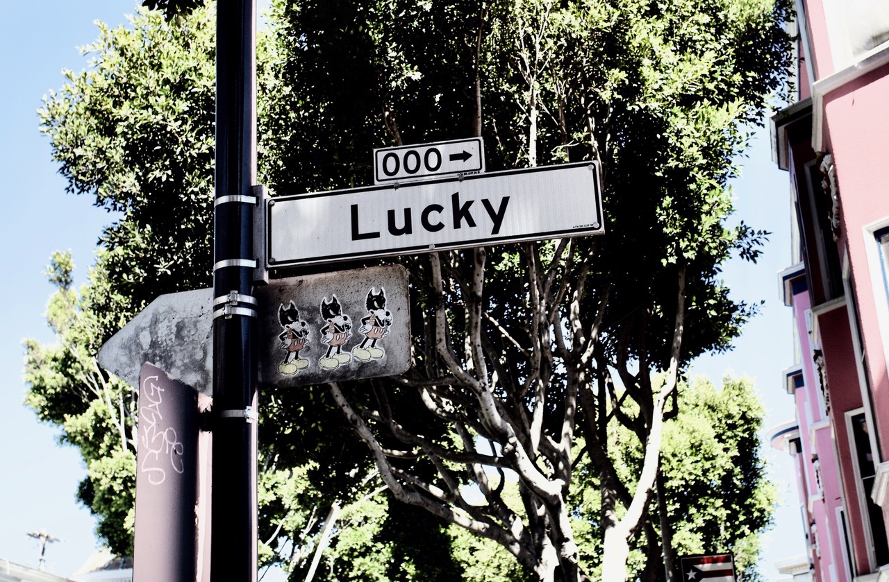A street sign with the name Lucky and trees in the background.