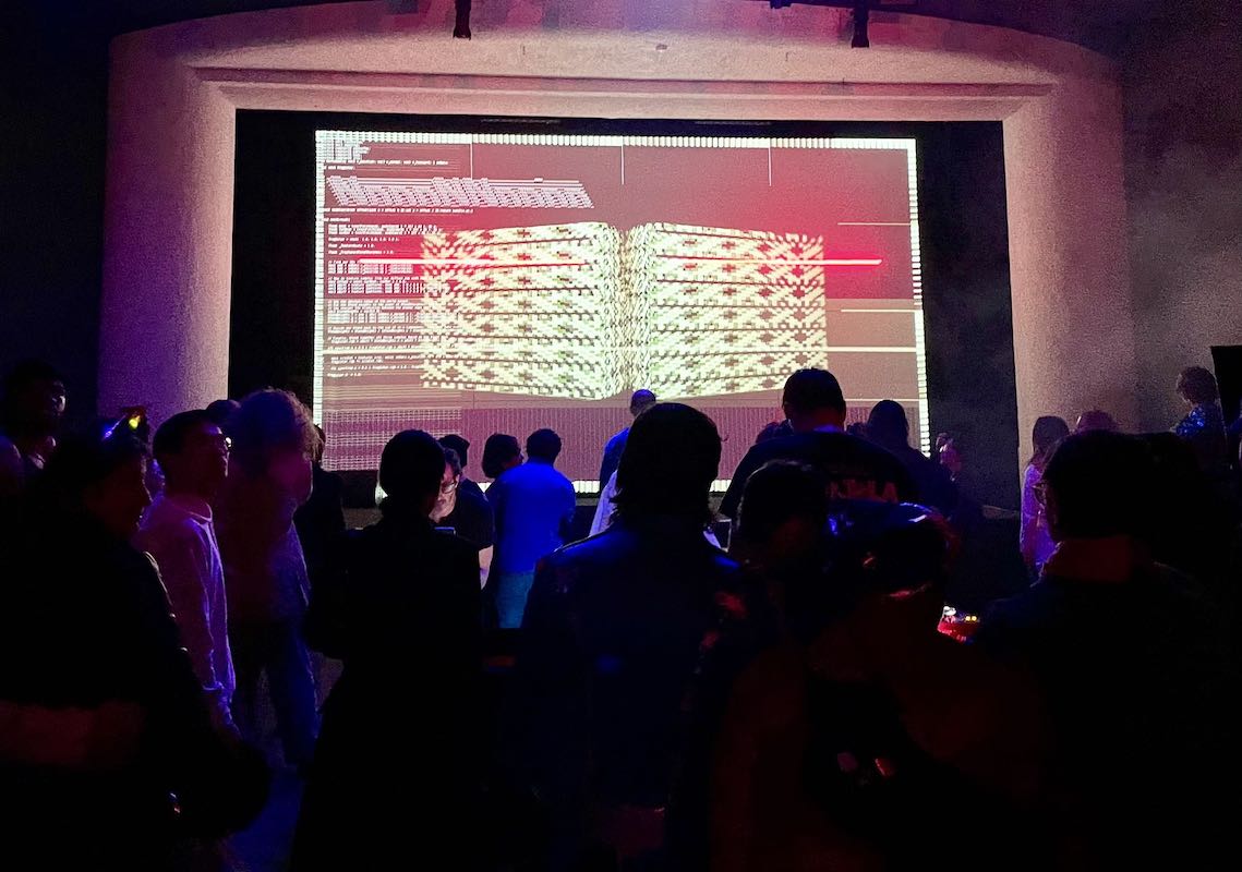 An AV club algorave in front of a large screen.