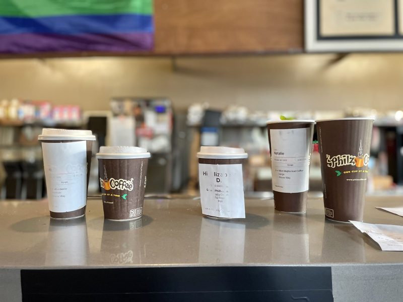 A line of Philz coffee cups on a counter with an lgbt flag.