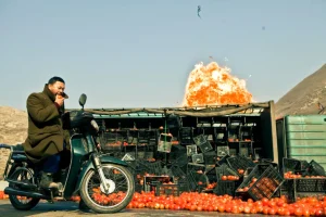 A man riding a motorcycle near a pile of oranges.