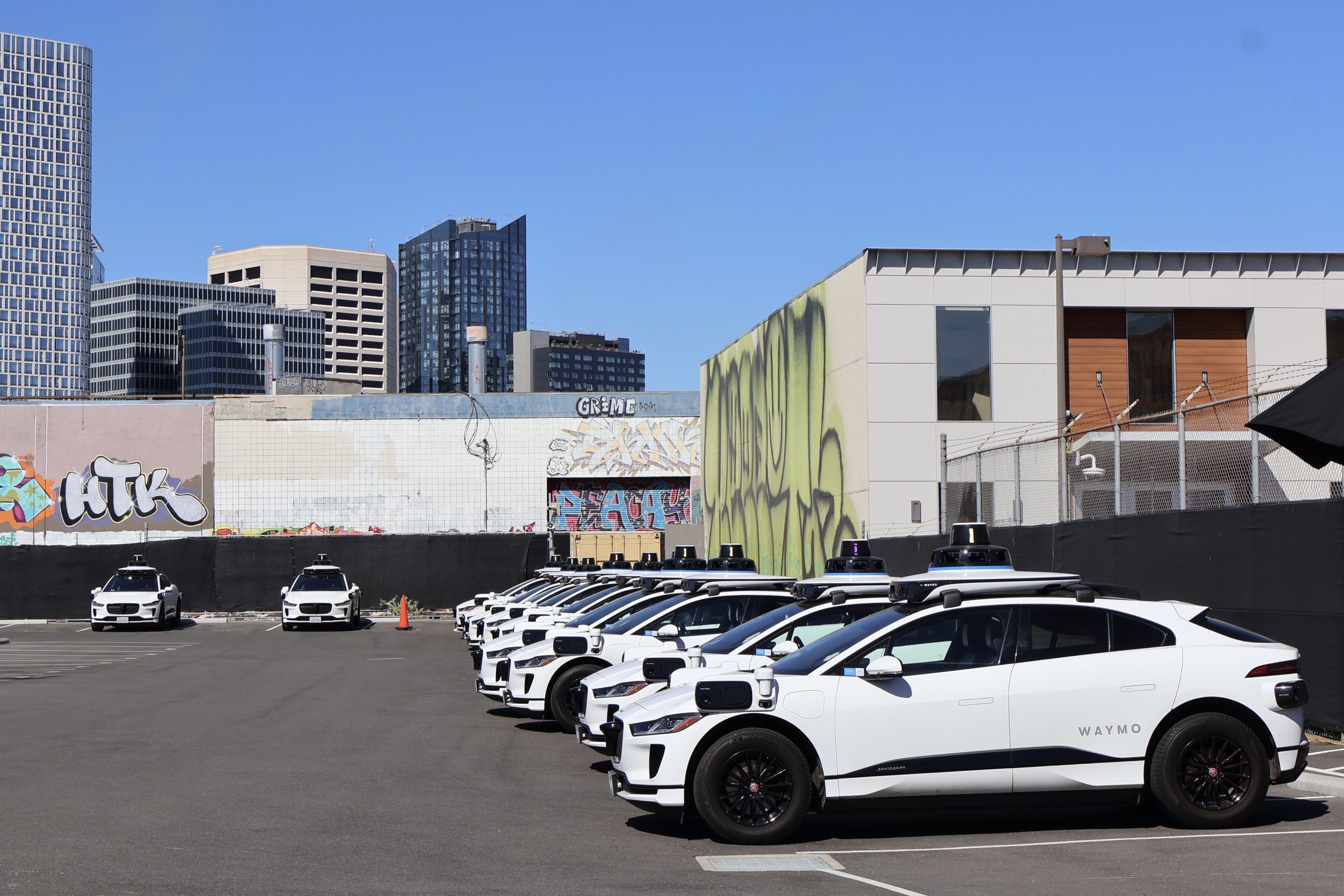 A group of Waymo cars parked in a parking lot.