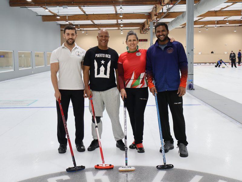 Four people posing for a picture in a curling rink.