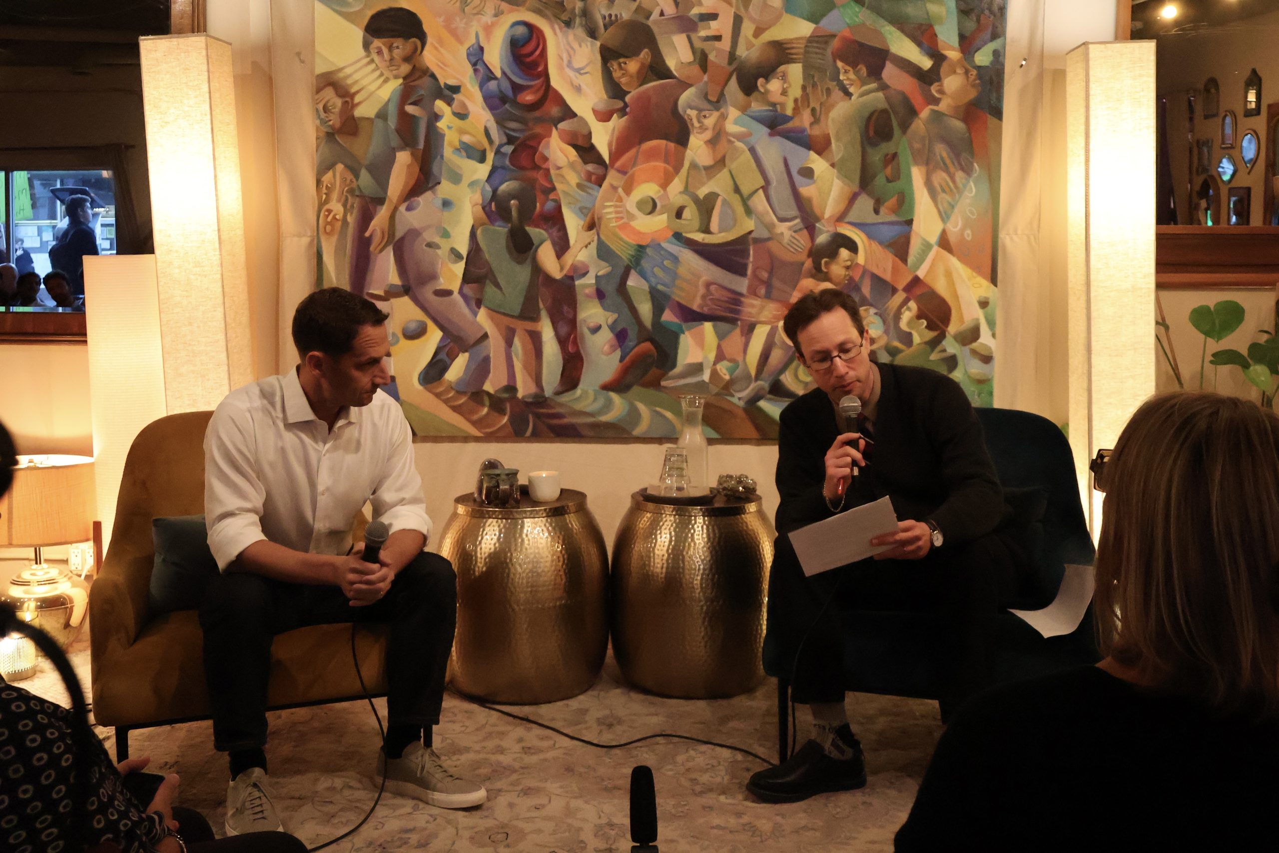 Two men sitting in chairs in front of a painting.