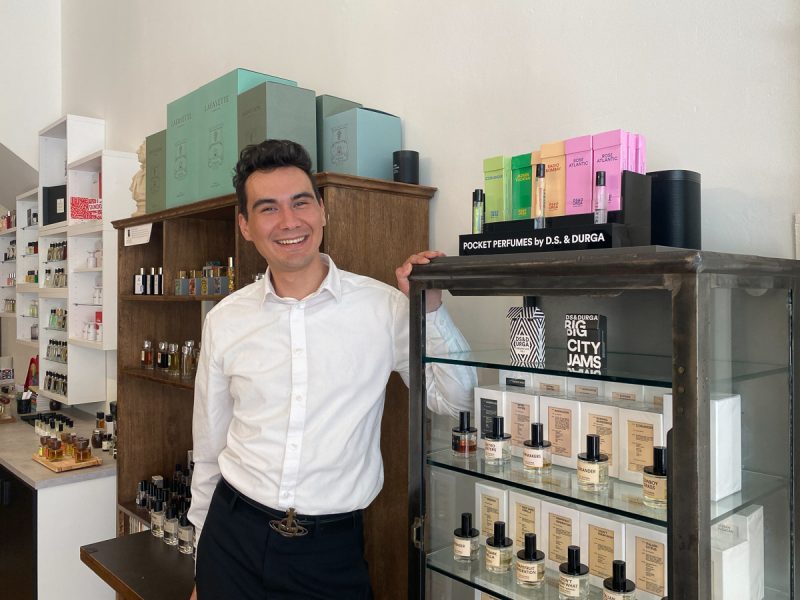 A man standing in front of a display case of perfumes.