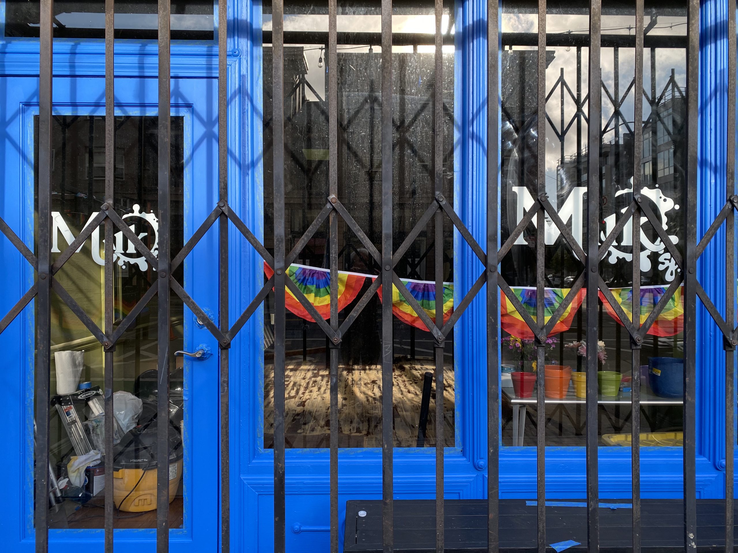 A blue storefront with a rainbow flag garland hanging from it.