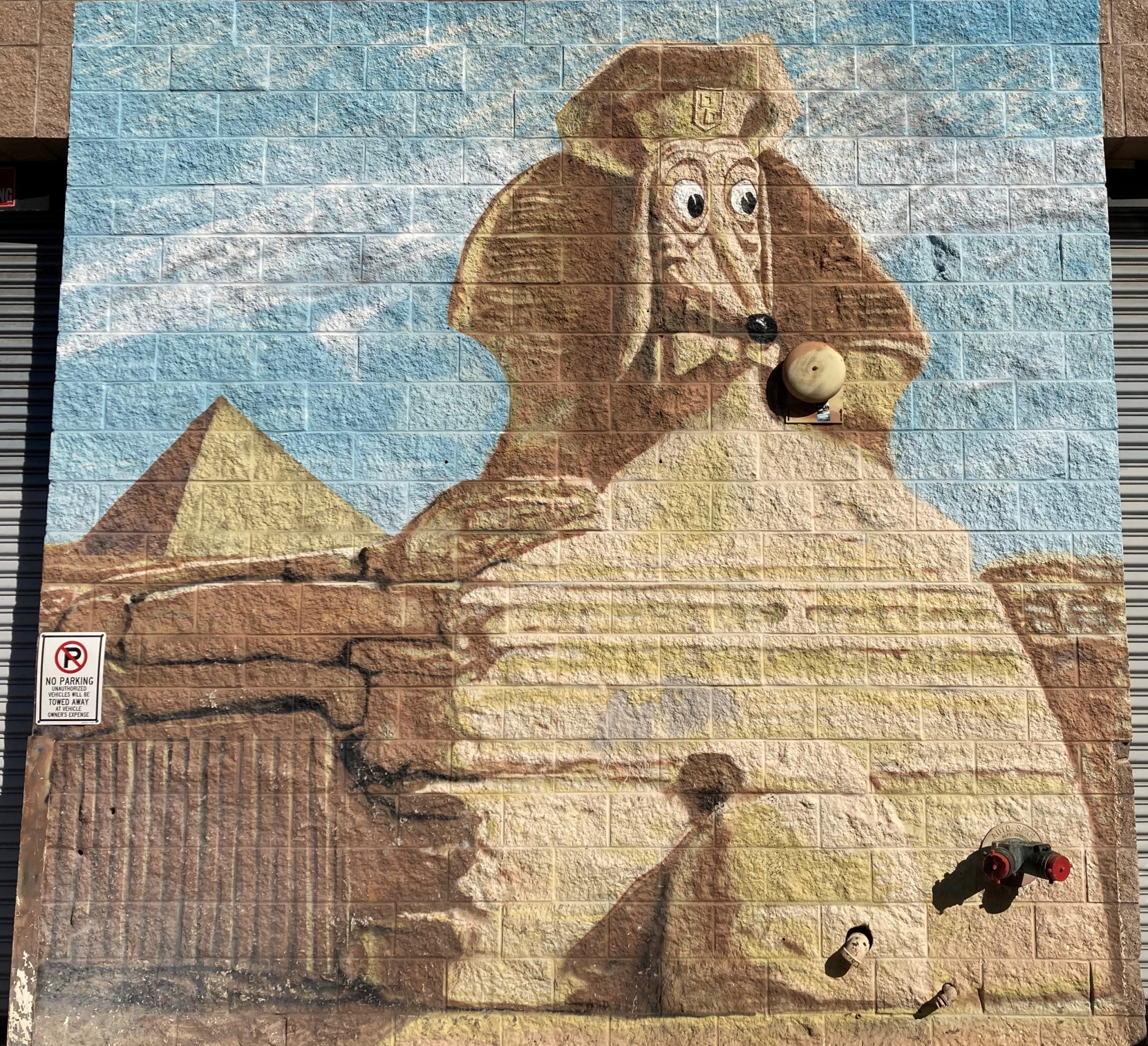 A mural of an Egyptian sphinx with a dog face on the side of a building.