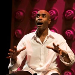 A man in a white shirt is sitting on a stage.
