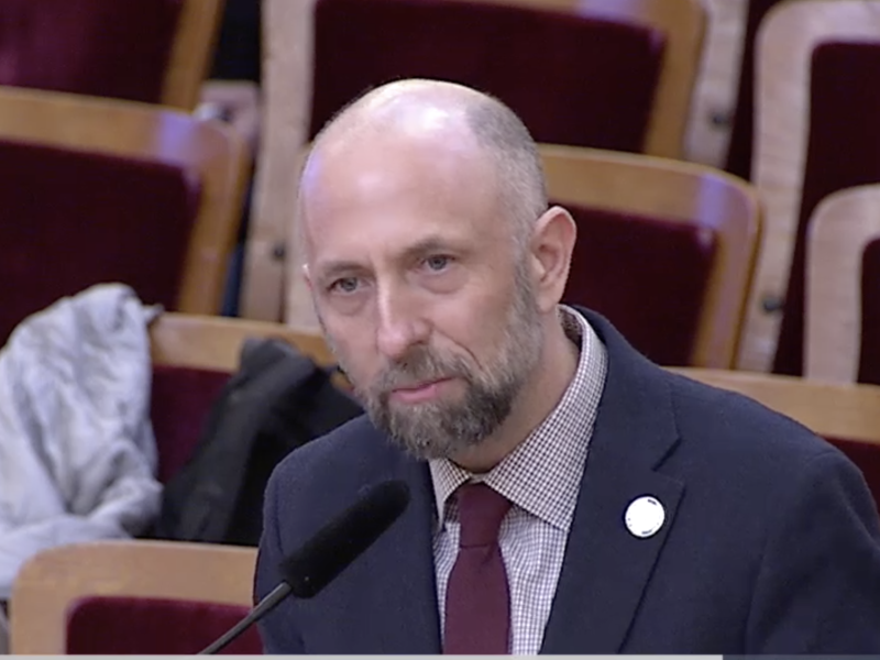 A bald man in a suit speaking into a microphone.
