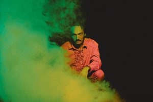 A man in a pink shirt sitting in front of a green smoke.