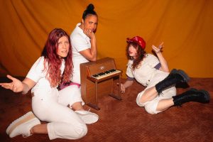 Three women posing in front of a piano.