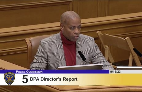 A man in a suit sits at a desk in a courtroom.