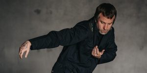 A man in a black jacket with his arms outstretched.