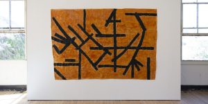 An orange and black piece of art hanging on a wall.