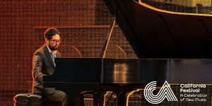 A man playing a piano in front of an orange background.