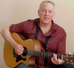 A man in a red shirt playing an acoustic guitar.