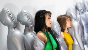 A group of women standing next to a row of silver mannequins.