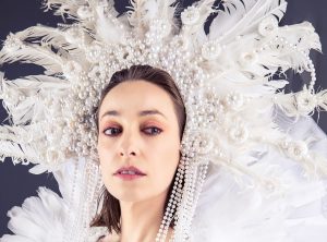 A woman in a white costume with feathers and pearls.