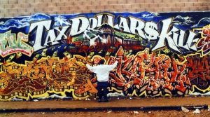 A man standing in front of a wall covered in graffiti.