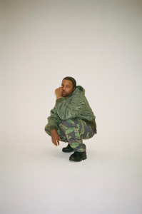 A man in camouflage pants crouching in front of a white background.
