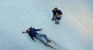 A man laying in the snow next to a woman.