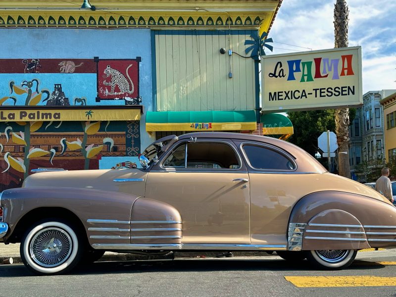 A vintage tan car parked in front of a restaurant.