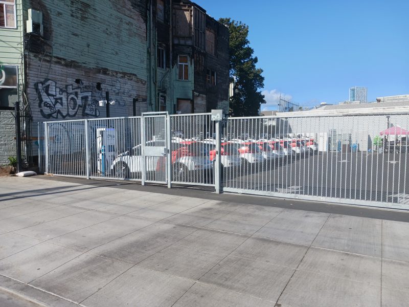 A fleet of Cruise cars parked in a parking lot behind a fence.