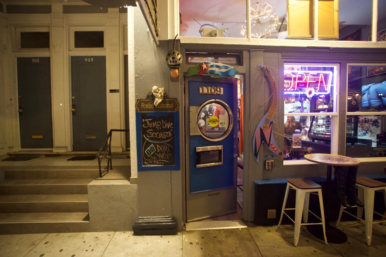 A bar with stools outside at night and with a sign that says "Jump, dive, socialize."