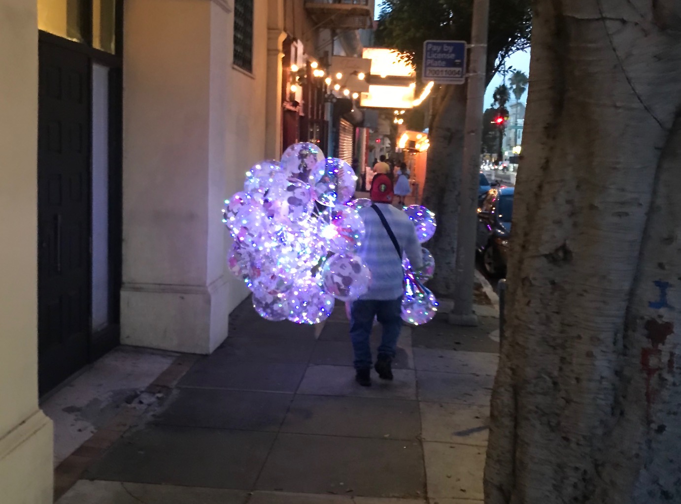 A person walking down a sidewalk with a large cluster of lighted ballons.