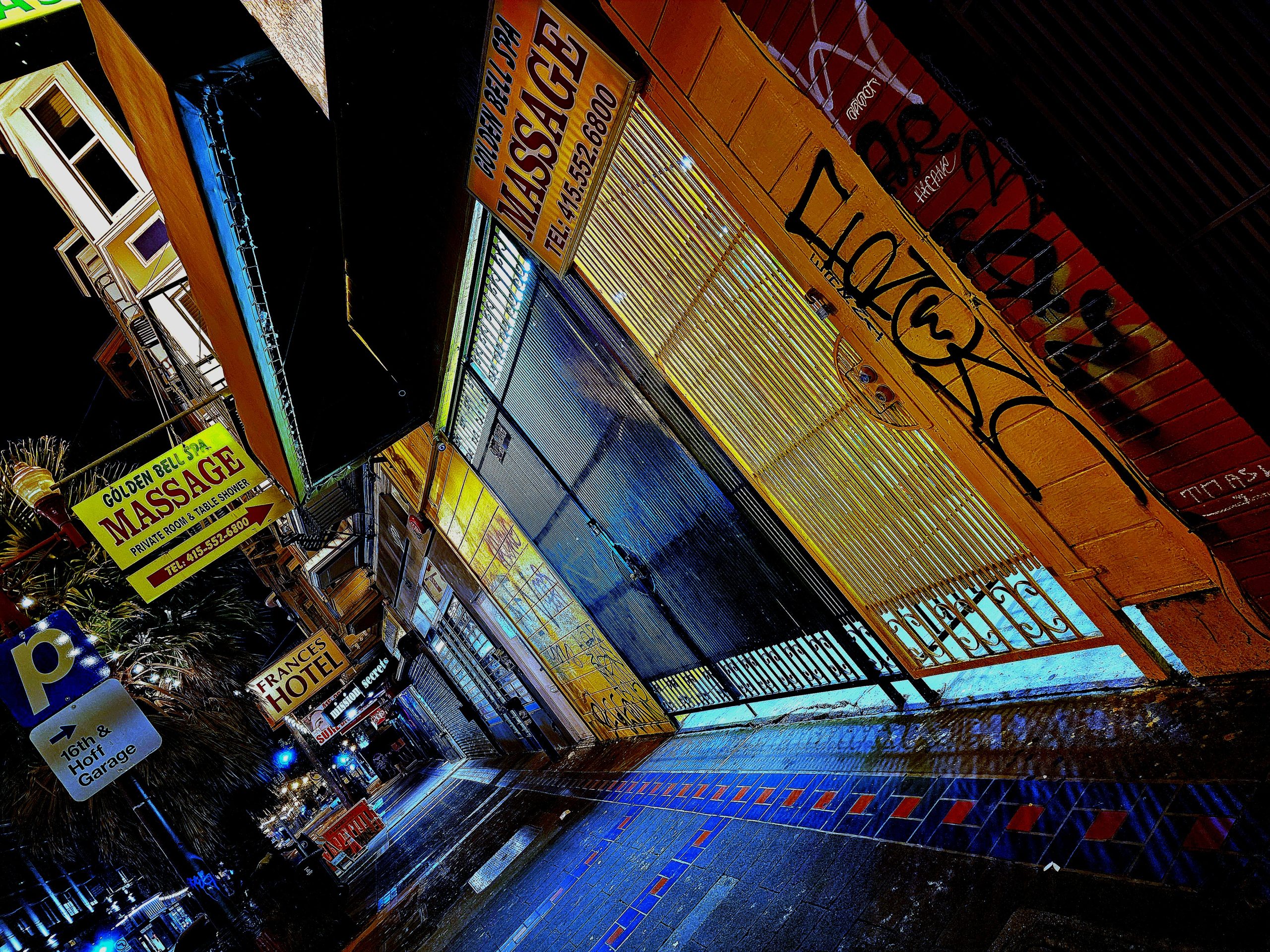 A city street at night with graffiti on the side of a building and a sign that says "Massage."