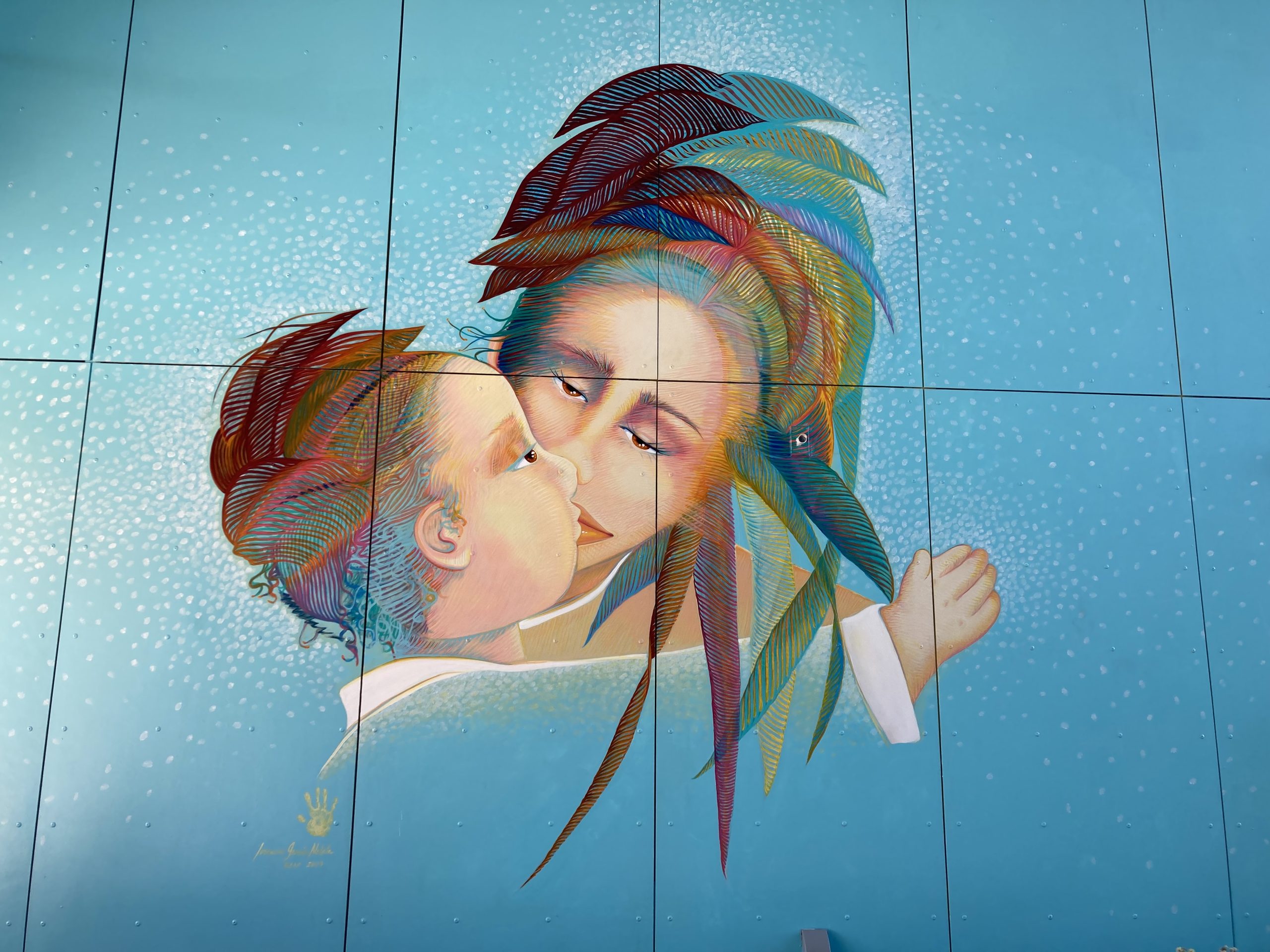 A painting on a wall, of a woman kissing a child.