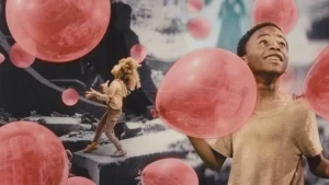 A boy is playing with pink balloons in front of a wall.