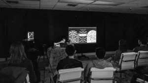 A black and white photo of a group of people watching a presentation.