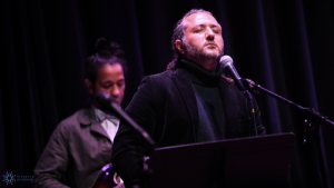 A man singing into a microphone next to another man.