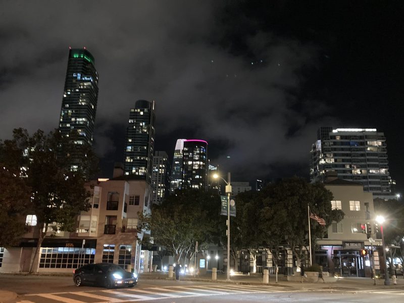 A city street at night with tall buildings in the background.