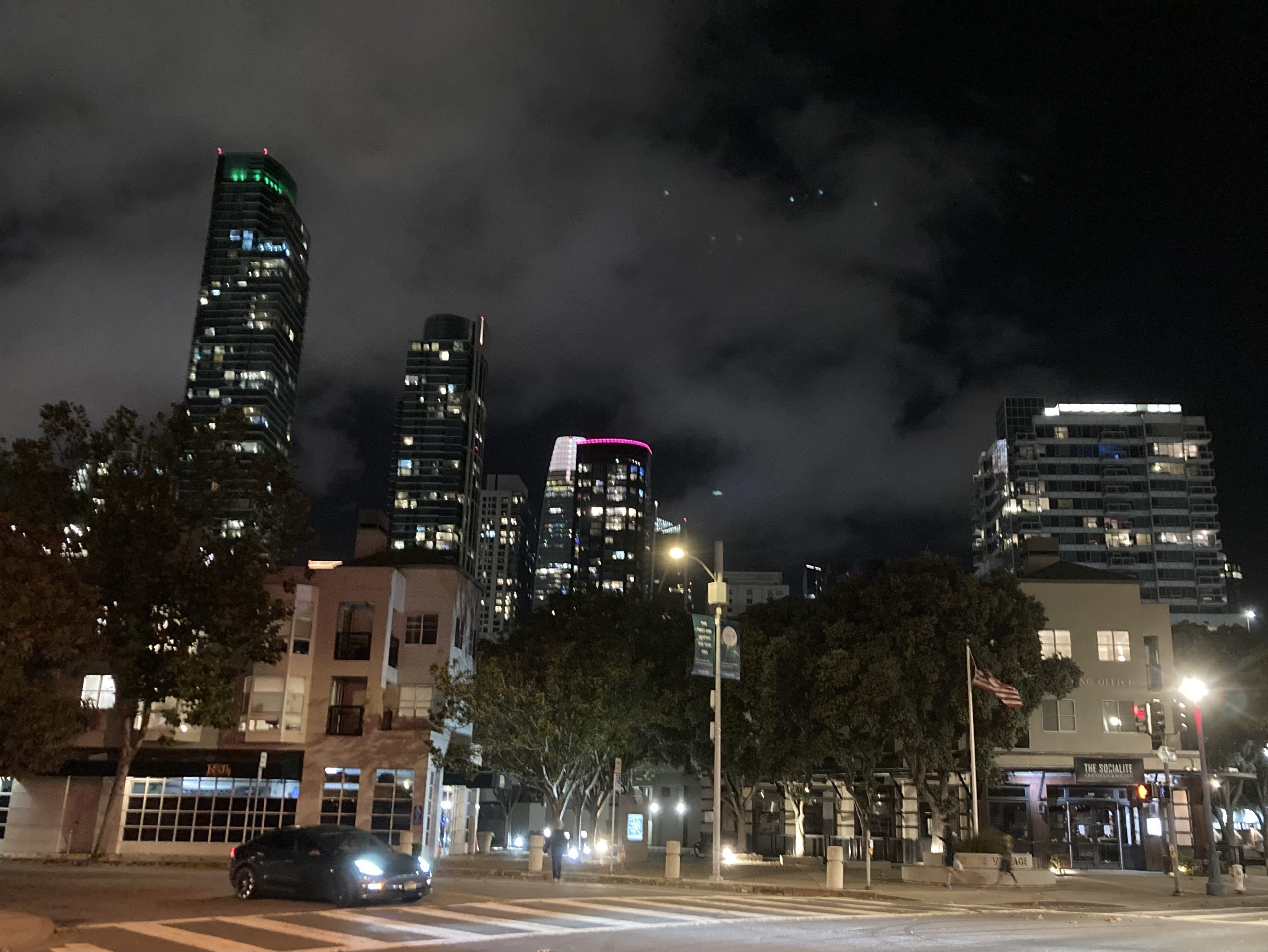 A city street at night with tall buildings in the background.