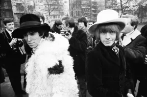 Two people wearing fur coats and hats in front of a crowd.