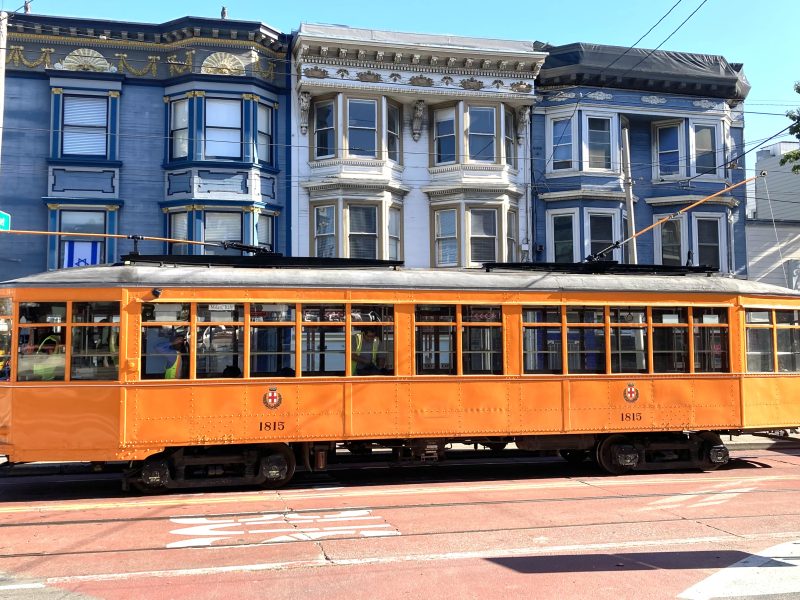 A yellow trolley car on a street in San Francisco.