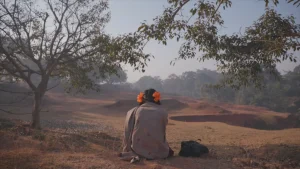 A woman sits on a hill looking at a field.