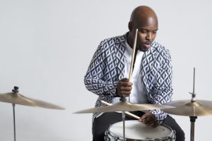 A black man playing drums on a white background.