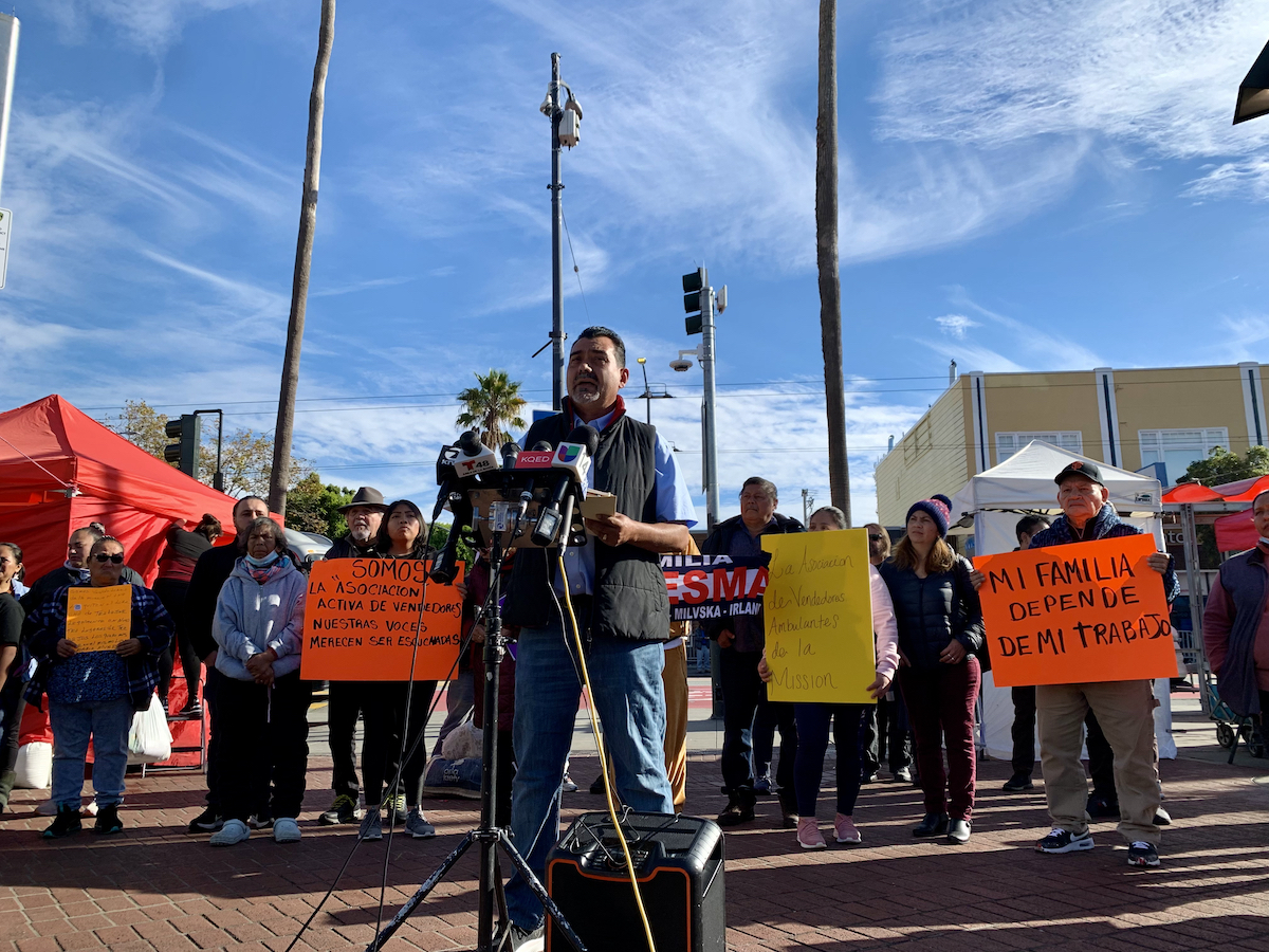 A group of people holding signs. A man front of a microphone.