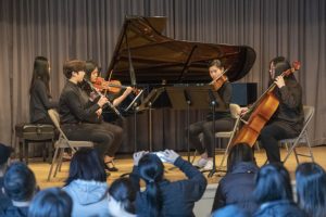 A group of people playing violin and cello in front of an audience.
