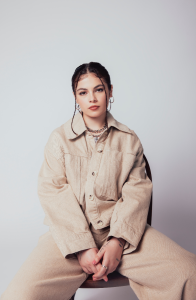 A woman in a beige jacket sitting on a chair.