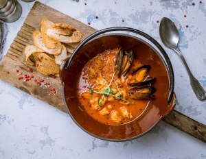 A pot of stew with mussels and bread on a table.
