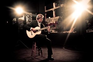 A man in a suit playing an acoustic guitar.