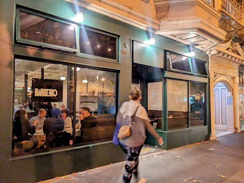 A woman walks past a restaurant at night.