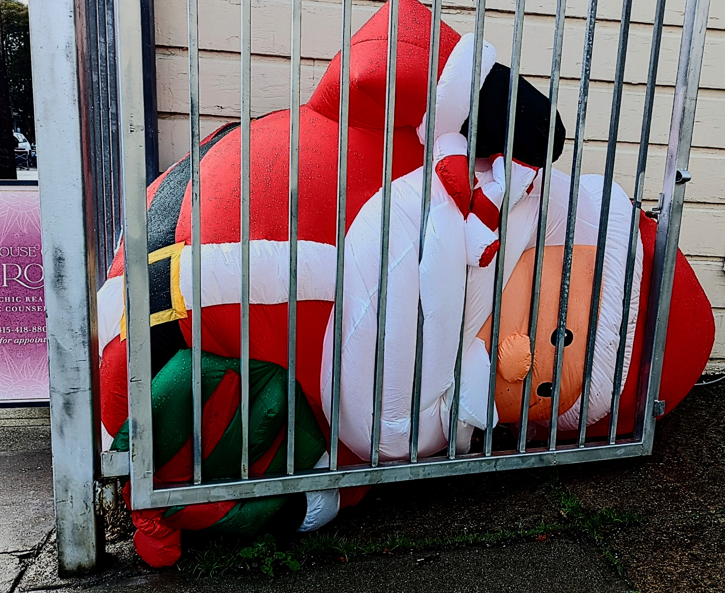 A large inflatable Santa Claus lying behind a fence.