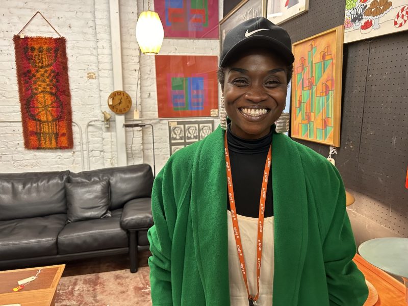 A smiling woman in a green coat standing in a room.