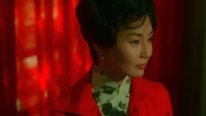 A woman in a red jacket standing in front of a red curtain.